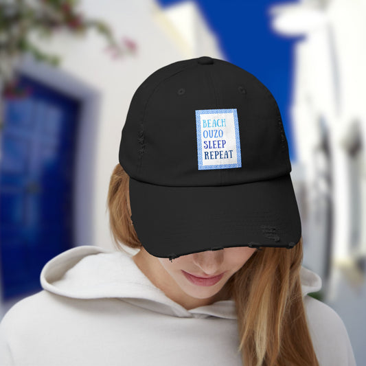 A model smiles wearing the black Ouzo hat with the funny quote "Beach, Ouzo, Sleep, Repeat." A great Ouzo gift and a stylish piece of Greek islands wear.