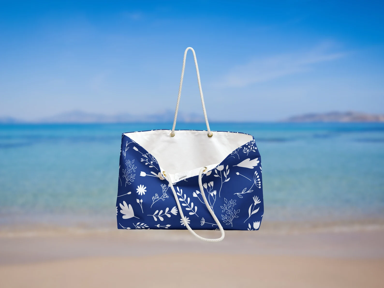The open bag reveals its cream-lined interior, emphasizing its storage capacity. Ideal as a beach bag with rope handles, the interior is roomy enough to hold weekend getaway items. This blue summer bag is made for travel to Greece or everyday summer adventures in the sun.