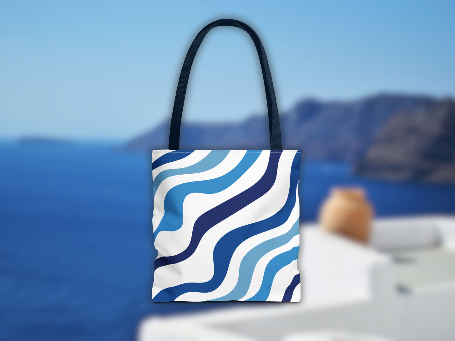 The blue bag in a Santorini setting. The image shows the stripes of the shoulder bag in different shades of blue and the blue color of the handles, an ideal bag for your summer vacation in Greece to complete your Santorini outfit