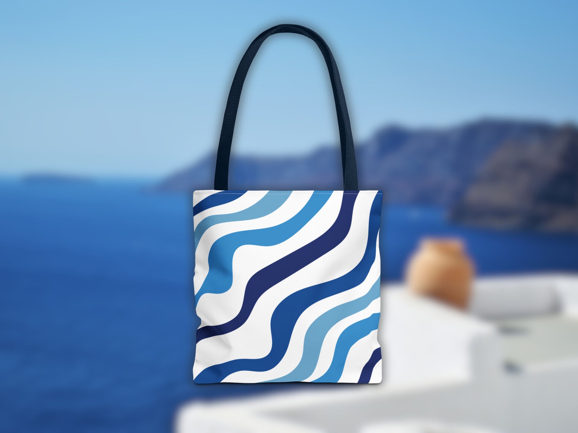 The blue bag in a Santorini setting. The image shows the stripes of the shoulder bag in different shades of blue and the blue color of the handles, an ideal bag for your summer vacation in Greece to complete your Santorini outfit