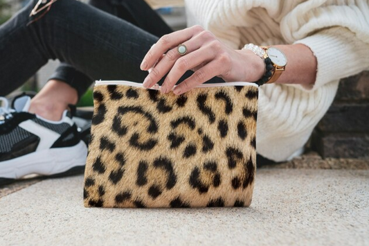 A woman holding the leopard purse, demonstrating its compact size and ease of carrying. This faux leather bag with its zip top clutch is a versatile animal clutch, ideal for on the go fashion. It is a stylish accessory.